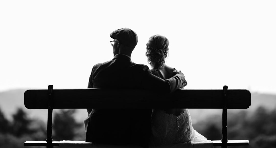 couple sitting on bench under tree grayscale photography